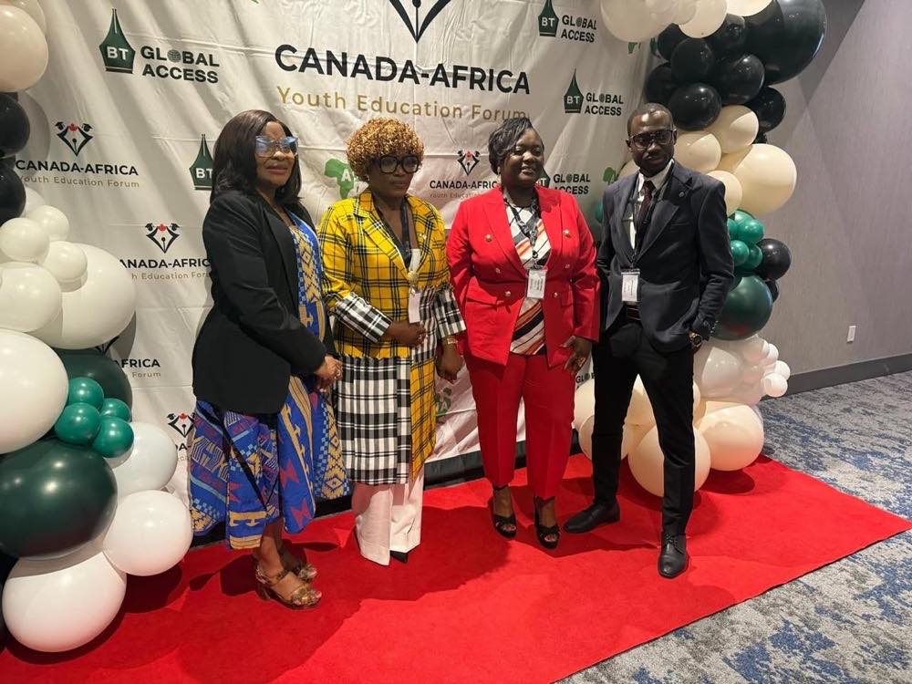 Quatre délégués posent ensemble sur un tapis rouge devant une toile de fond du Forum canado-africain sur l'éducation des jeunes, encadrés par des ballons verts, noirs et blancs.